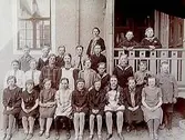 Rynninge folkskola, 25 skolbarn med lärare fröken Mossberg.
Skolbyggnad i bakgrunden.