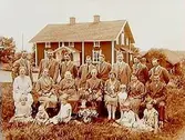 En och en halvvånings bostadshus med förstebro och förstuga. Släktgrupp 21 personer framför huset.
Gustaf Larsson