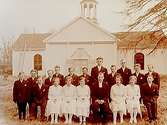 Konfirmander, 5 flickor, 13 pojkar och pastor A. Swahn.Boo kyrka i bakgrunden.