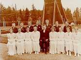 Konfirmander, 8 flickor, 7 pojkar och pastor Bertil Eriksson.
Mullhyttemo kyrka i bakgrunden.