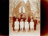 Längbro kyrka i bakgrunden
Konfirmander, 4 flickor, 5 pojkar och kyrkoadjunkt K. E. Hagberg.