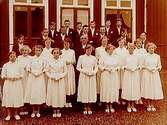 Glanshammars kyrka.
Konfirmander, 13 flickor, 13 pojkar och kyrkoherde Gunnar Johansson.
Bostadshus i bakgrunden.