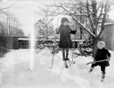 Skidåkning, två barn.
Ingrid Lindskog på skidor och Sven Lindskog med spade.