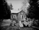 Bostadshus, släktgrupp 9 personer framför huset.
Knut Albin Blyckerts 70 årsdag. Han är född 1864.
Med på bilden bl.a. Carolina Mathilda Schöllin (Sam Lindskogs moster Tilda), Sam Lindskog och hans hustru Hulda Lindskog.
Mannen längst till höger är Tildas och Knut Albins son, Sven Blüchert. Kvinnan stående i mitten är Stina Blüchert, Sven Blücherts dotter.
Mannen sittande till höger på bilden kan vara Oskar Johansson (Tildas son) och kvinnan sittande till höger kan vara Oskars fru.
Kvinnan längst till vänster är troligen Selma (gift Andersson), Sam Lindskogs syster.