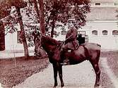 En man till häst.Bostadshus i bakgrunden.G. Börjesson
