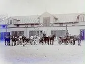 Stallbyggnad. Två hästdroskor med kuskar. En landå med en häst. En man med två hästar. En newfoundlandshund.
G. Sandholm
