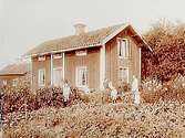 En och en halvvånings bostadshus (parstuga ?).
Familj 7 personer framför huset.
Gustaf Lindén