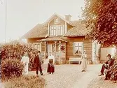 En och en halvplans bostadshus med frontespis, veranda. Köksingång.
5 personer framför huset.
Edvind Olsson.