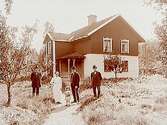 Tvåvånings bostadshus med veranda och trapphus.
3 män, en kvinna och ett barn framför huset.
Ernst Pettersson.