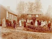 Tvåvånings enkelstuga. En flygelbyggnad.
13 personer framför byggnaderna.
Karl Åkerstrand.