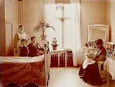 Sovrumsinteriör.
2 småbarn, en sköterska och 2 kvinnor.
Köpman Ludvig Morén.
Dalarna.
