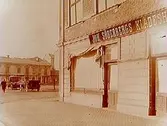 Tvåvånings bostadshus med affärslokaler i bottenvåningen, Joh. Söderbergs Klädeshandel.
Två automobiler på Järntorget.
Teaterdirektör Liander
