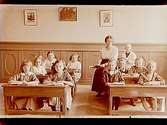Stora Mellösa skola, klassrumsinteriör, 10 skolbarn i sina bänkar och lärarinnan.
Skollärare fröken Barr.