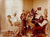 Rumsinteriör.
Familj 6 personer vid orgeln, far spelar fiol.
J.A. Boo