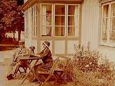 En man och en kvinna med en tax vid bordet, framför huset.
K.E. Malmström