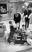 Krämaren 5 år 26 mars 1968

Krämaren firar 5 år som butik. På bilden ser man två män i kostym som delar ut spargrisar till barnen. Två pojkar sitter i trampbilar med ballonger, och en flicka sitter på en gunghäst, och en annan flicka har en dockvagn.