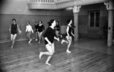 Motionsgymnastik 9 april 1968

Kvinnor springer i en gymnastiksal. De har gymnastikdräkt på sig, men en har långbyxor och en vit jacka. På bilden syns också en balkong.