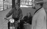 Motorcyklar 30 april 1968

En man kör en motorcykel med sidovagn och i den sitter en kvinna. Framför dem har det stannat en kvinna, klädd i kappa och hatt. I bakgrunden ser man en cyklist och bil.