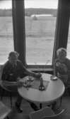 Ånnaboda 27 april 1968

En man och en kvinna sitter vid ett runt bord och dricker kaffe på Ånnaboda servering. Man kan se Ånnaboda sjön genom fönstret bakom dem och en Majbrasa.