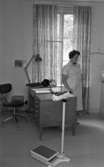 Barnavårdslokalen i Lillån 14 september 1966

En distriktsköterska står vid ett skrivbord och tittar på något. På bilden ser man en också en personvåg.