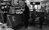 Baronbackens centrum 2 december 1966

En man i rock står vid kassan och skall betala. Två barn i jacka med luva står bakom honom och tittar på godis.