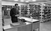 Bibliotek 10 februari 1967

En man i mörk kostym och glasögon arbetar på biblioteket. På bilden ser man hyllor med böcker.