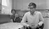 Gyttorp 23 februari 1967

En kvinna sitter med ett barn i famnen vid ett bord i köket. En man med glasögon och vit skjorta sitter också vid bordet.
