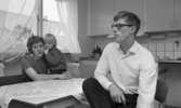 Gyttorp 23 februari 1967

En kvinna sitter med ett barn i famnen vid ett bord i köket. Det sittter också en man med glasögon och vit skjorta vid bordet.