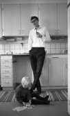 Gyttorp 23 februari 1967

En man med glasögon och vit skjorta står vid diskbänken och röker pipa. Framför honom sitter en flicka på mattan och leker med en kortlek.