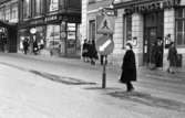 Gående, första felgångarn 7 februari 1967

En kvinna går vid ett övergångsställ. Bakom henne ser man Göteborgs Bank, och Oscaria skoaffär.