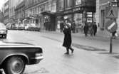 Gående, första felgångarn 7 februari 1967

En kvinna går över övergångsstället, och man ser bilar parkerade på gatan.
