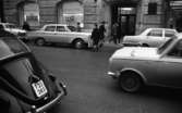 Gående, första felgångarn 7 februari 1967

Utanför Skandinaviska Banken står det bilar parkerade, och så ser man en bil kommer åkande.