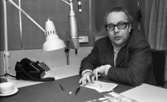 Carl-Uno Sjöblom 24 december 1968

Programmledaren Carl-Uno Sjöblom sitter vid ett bord i en studio med en penna i handen. Framför honom ser man en mikrofon, lampa och en telefon.