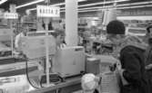 På ICA Norahallen sitter en kassörska i kassan i randig arbetsklädsel. En kvinna i kappa med rutigt foder står 
vid kassan med ett barn. På bilden ser man några kunder till.
8 mars 1967