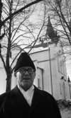 Landgren Kommunnummer 8 mars 1967

Kyrkans kontraktprost Enar Landgren står framför kyrkan. Han är klädd i rock, vit halsduk och pälsmössa.
Han har också glasögon.