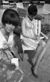 Systrarna Rynning igen, 7 juli 1965
Grythyttan utemöbler. 
Två kvinnor sitter utomhus på varsin stol. De är klädda i varsin sommarklänning. De har papper och pennor i sina händer. Båda kvinnorna skriver. Kvinnan till vänster i förgrunden har en rosett vid barmen utanpå klänningen samt en fluffig, kort frisyr. Den andra kvinnan har en randig klänning samt kortklippt hår. Hon har pumps på fötterna.