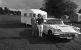 Camping 5 juli 1965.

Familj bestående av mor, far och liten flicka stående vid bil med husvagn på tältplats.