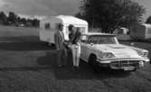 Camping 5 juli 1965.

Familj bestående av mor, far och liten flicka stående intill bil med husvagn på tältplats.