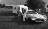 Camping 5 juli 1965.

Familj bestående av mor, far och liten flicka stående intill bil med husvagn på tältplats.