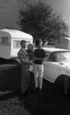Camping 5 juli 1965.

En familj bestående av mor, far och liten flicka stående vid bil med husvagn på tältplats.
