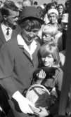 Knytkalaset 5 juli 1965.

En jubileumsvärdinna med en liten flicka. De håller gemensamt i en korg och den lilla flickan har en kattunge i famnen. Åskådare i bakgrunden.