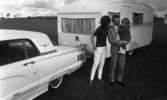 Camping 5 juli 1965.

Familj bestående av mor, far och liten flicka stående vid bil med husvagn.
