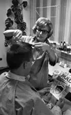 Damfrisörskor 8 juli 1965.

Damfrisörska klipper herre. Den senare studerar ett exemplar av serietidningen MAD under tiden.