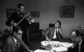 Knätofsmöte i Idrottshuset, 16 juli 1965.

Musiker i folkdräkt spelar fiol för tre herrar som har sammanträde på Idrottshuset.