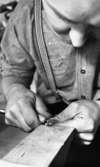 Silversmed 20 augusti 1965

En silversmed i arbete. Han håller ett verktyg i sin högra hand samt ett silverföremål i sin vänstra hand. Han bearbetar silverfiguren.