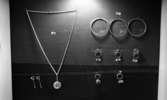 Silversmed 20 augusti 1965

En tavla med uppfästade silversmycken såsom örhängen, halsband, armband samt ringar till försäljning. Små prislappar hänger också på tavlan.