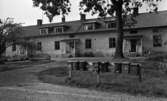 Hasselfors bruk 19 augusti 1965

Hus med flera bostäder i på Hasselfors bruk. Tre entrédörrar till huset syns på bilden. I förgrunden syns åtta postlådor uppsatta på ett trästaket. Två träd syns även på bilden.