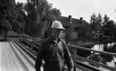 Hasselfors bruk 19 augusti 1965

En bruksarbetare i keps, skjorta samt byxor med hängslen går över en bro på Hasselfors bruk. I bakgrunden syns ett tegelhus.