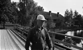 Hasselfors bruk 19 augusti 1965

En bruksarbetare i keps, skjorta samt byxor med hängslen går över en bro på Hasselfors bruk. I bakgrunden syns ett tegelhus.