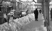 Halkiga pensionärer, 18 december 1965

I förgrunden syns en manlig pensionär med ryggen mot kameran. Han går på trottoaren på Drottninggatan. Vid sidan av trottoarkanten finns en snövall. Ur denna sticker parkeringsmätare upp. Bilar står parkerade längs med gatan invid trottoarkanten. Flera människor syns i bakgrunden. Längre fram på gatan hänger en skyltar med texterna 